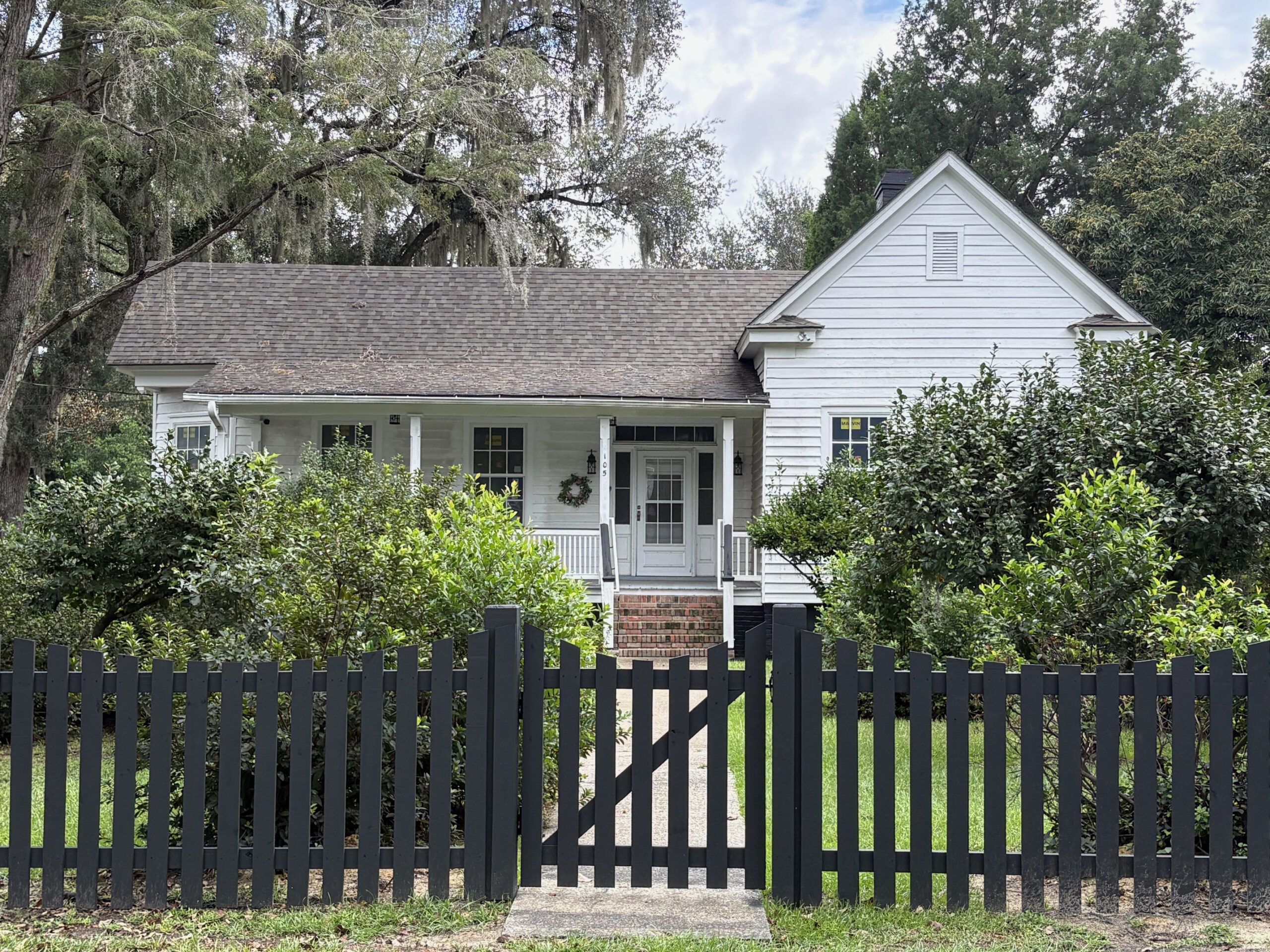 A white house surrounded by a black fence, featuring a gate at the front entrance