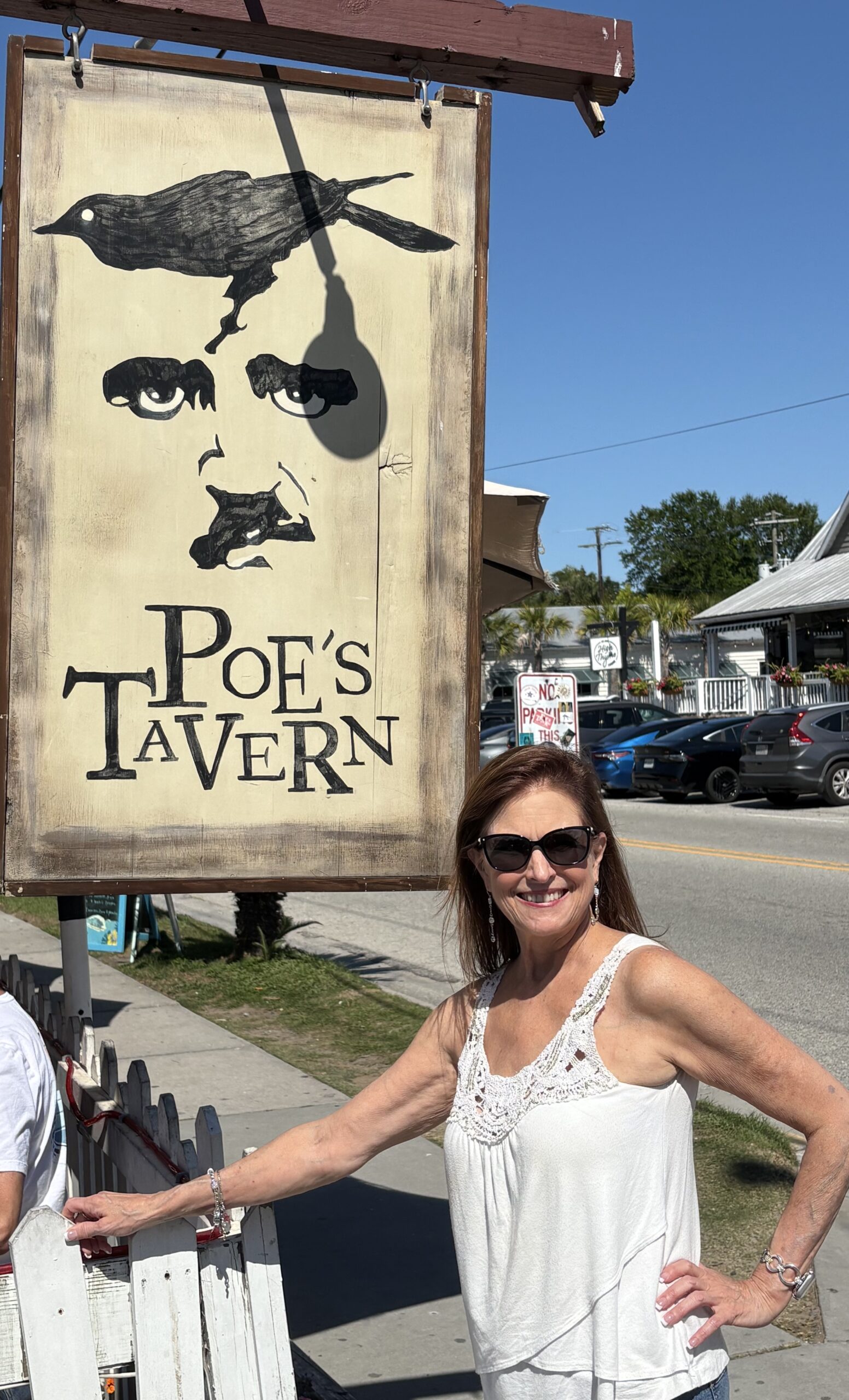A woman stands beside a sign reading "Poe's Tavern," showcasing the establishment's name and inviting atmosphere
